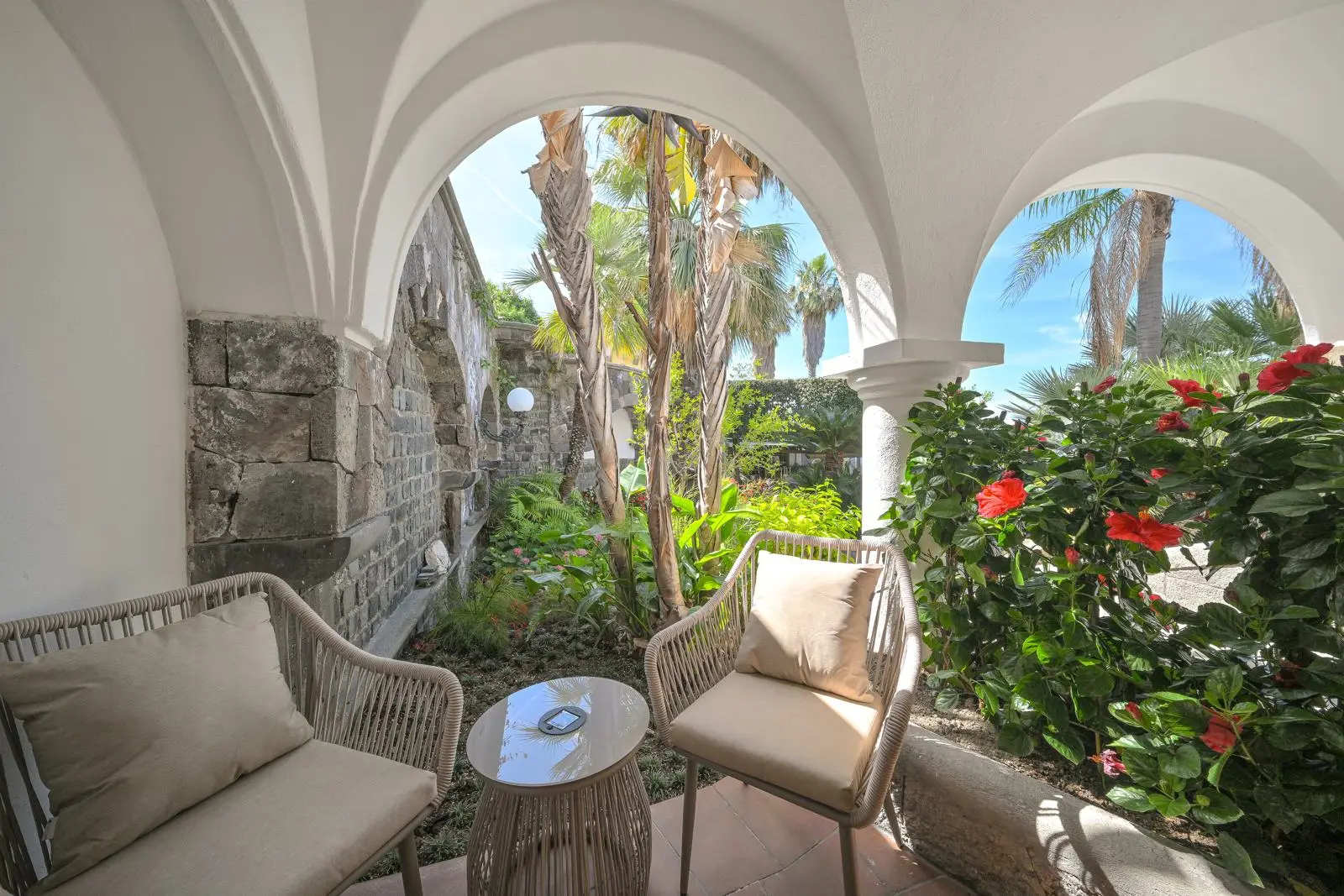 The stone patio with wicker armchairs beneath the arches